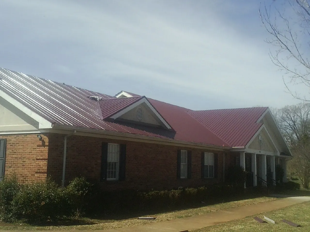 Red metal roof with gabled entries on a long brick building, from a Hail Damage Roof Repair job in Mattaponi