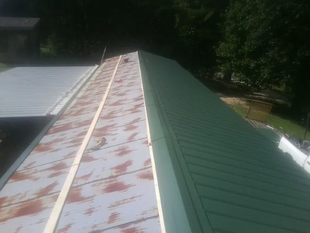 Old rusted panels beside newly installed green metal roofing — Wind Damage Roof Repair by Roofing Brothers in Mattaponi