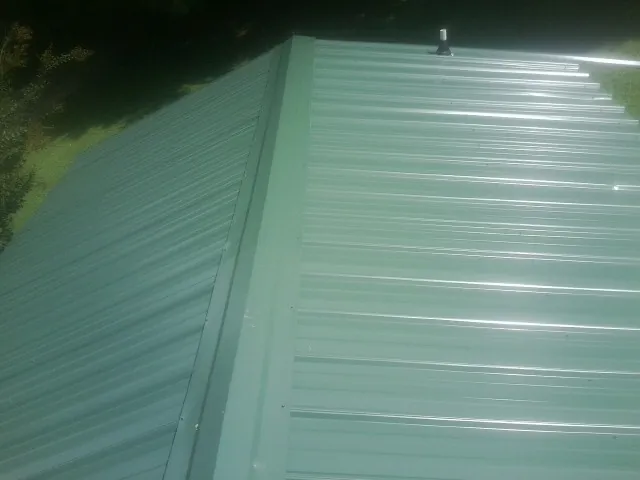 New green metal panels meeting at the ridge of a roof — Flat Roof Repair work by our crew in Mattaponi