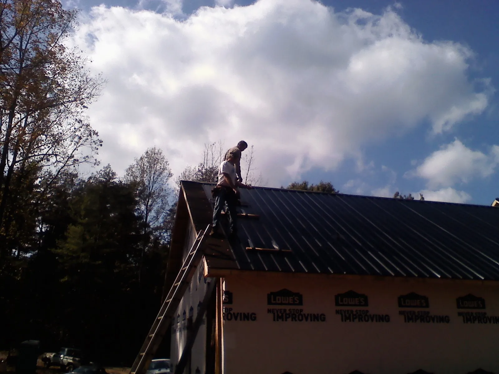 Roofer fastening dark metal panels high against a cloudy sky, from a Roof Inspection job in Mattaponi