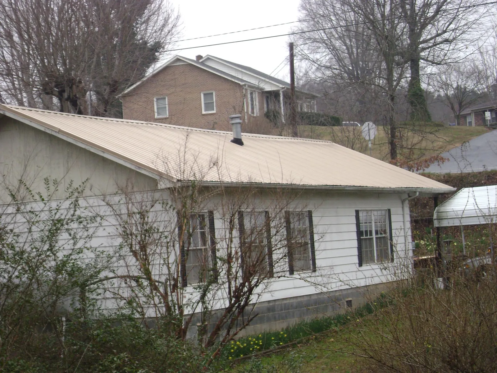 Tan metal roof on a white sided house set into a hillside — Commercial Roofing by Roofing Brothers in Mattaponi